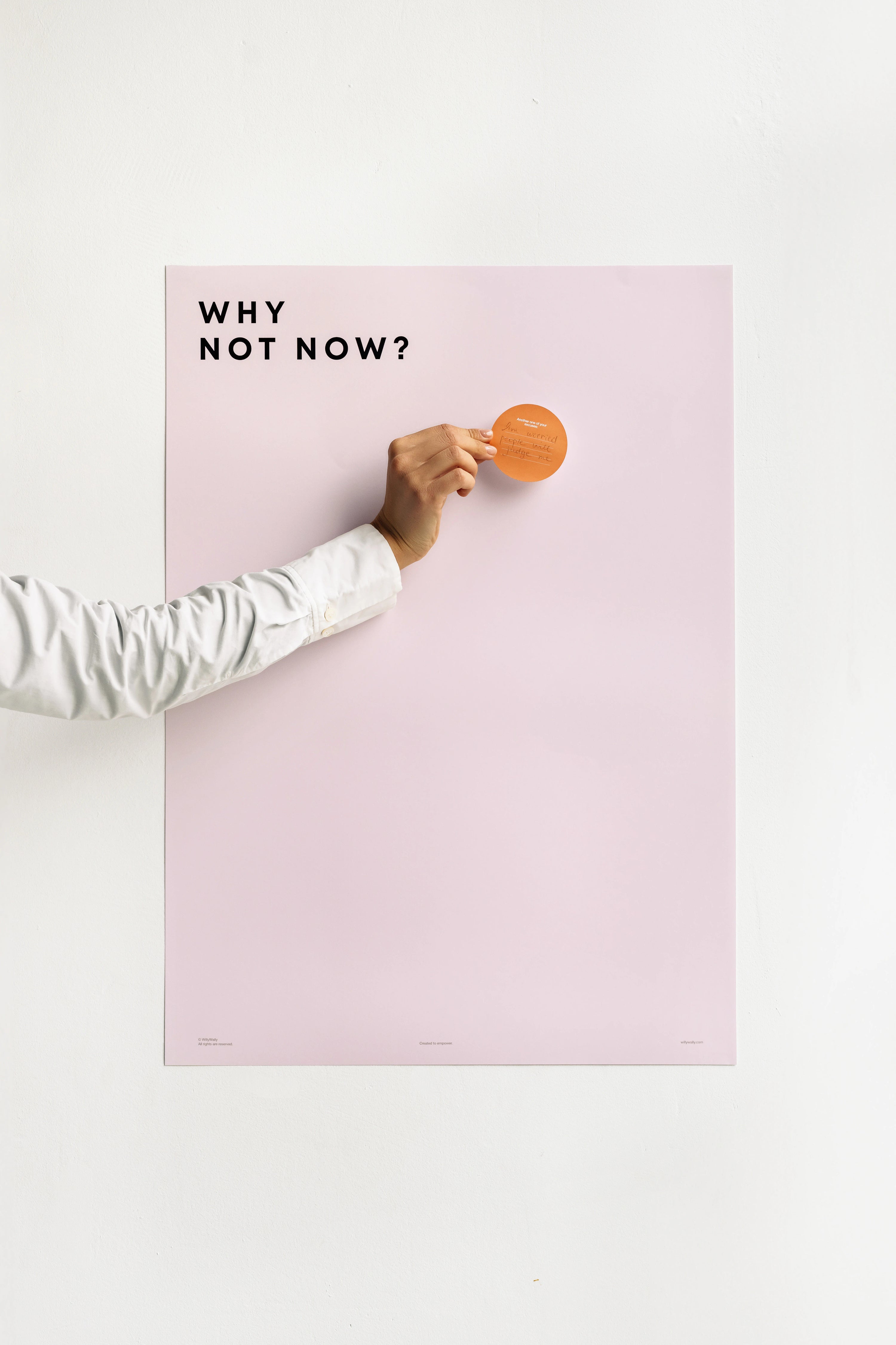 Hand pressing a button on a pink board with 'Why Not Now?' text