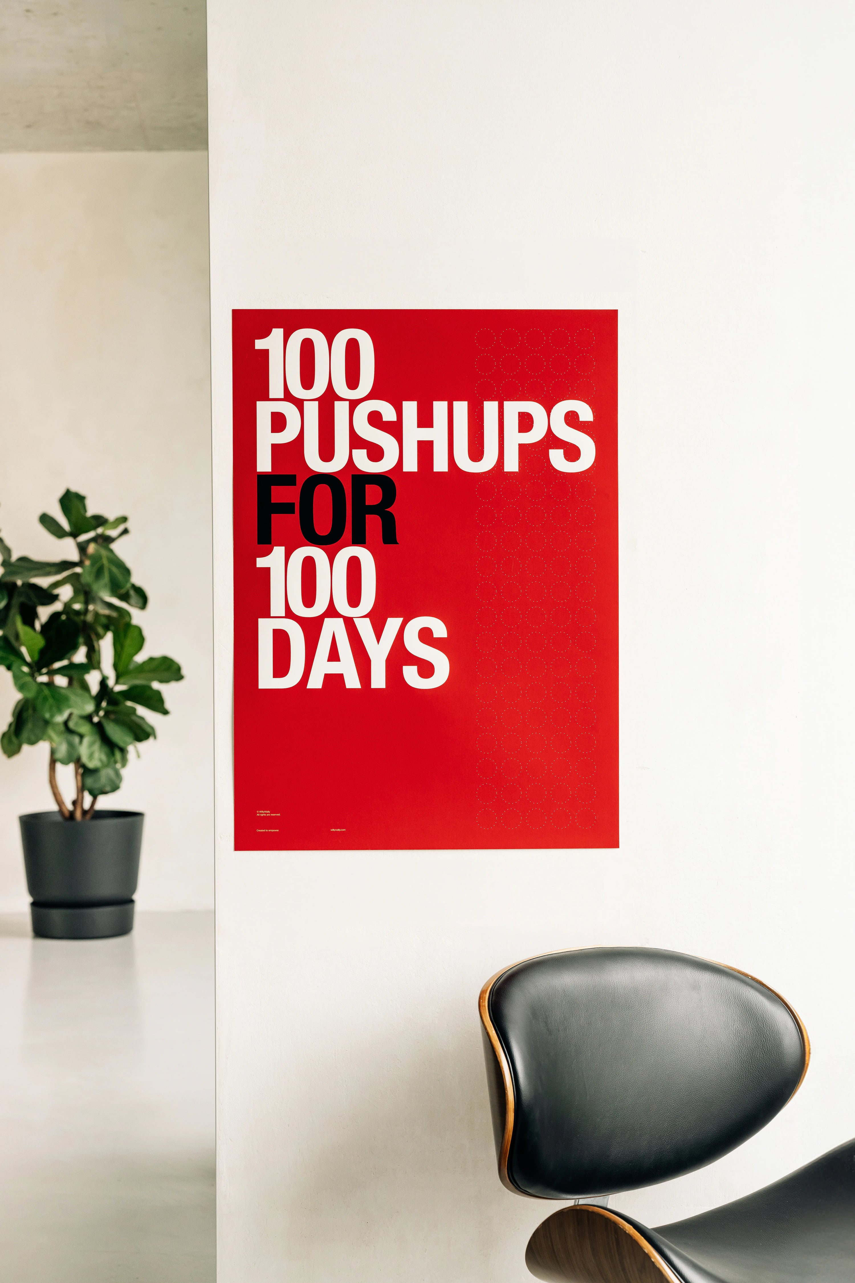 Poster with '100 Pushups for 100 Days' text on a red background in a room with a plant and chair.