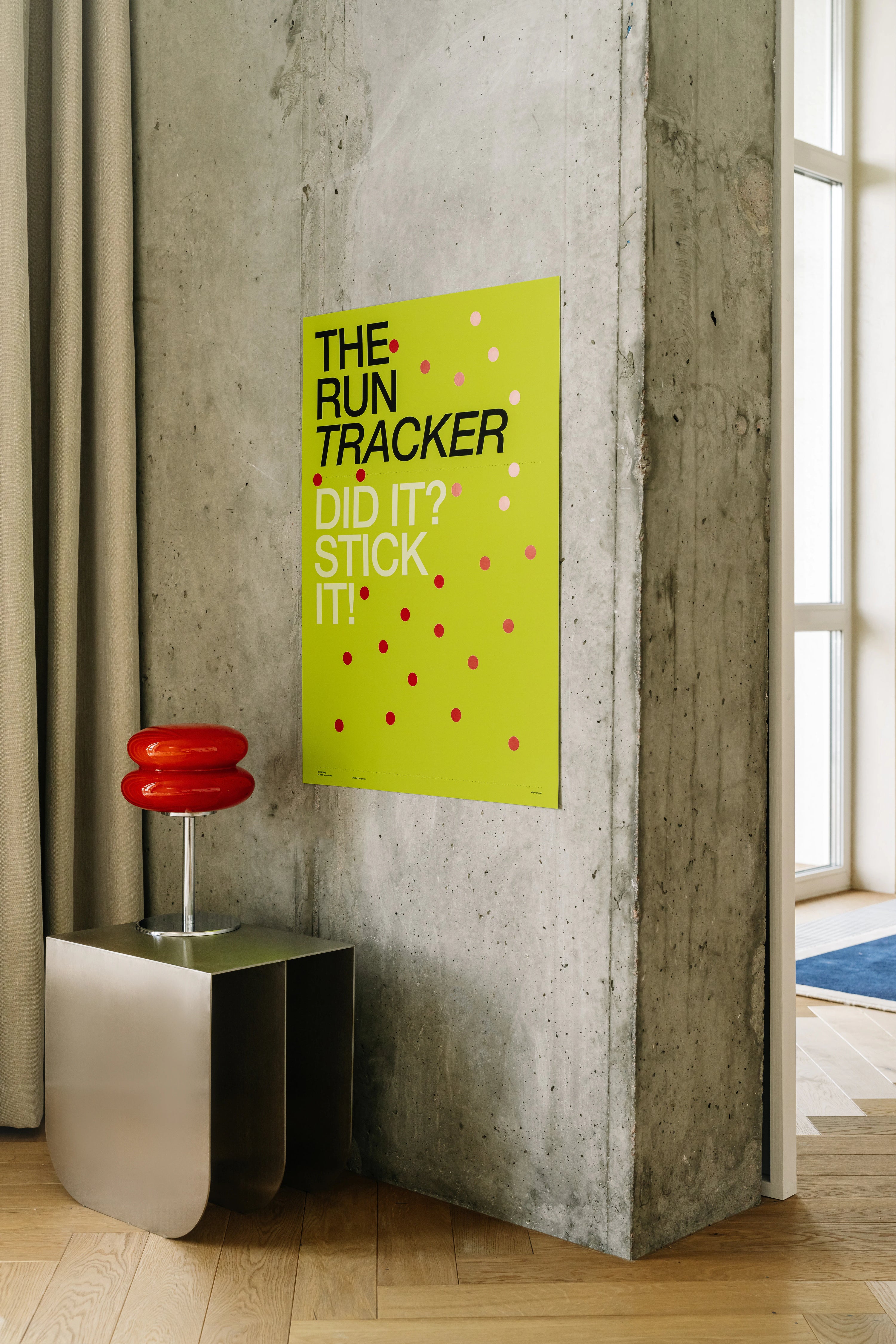 Poster with text on a wall next to a modern stool in a room with concrete walls and a window.