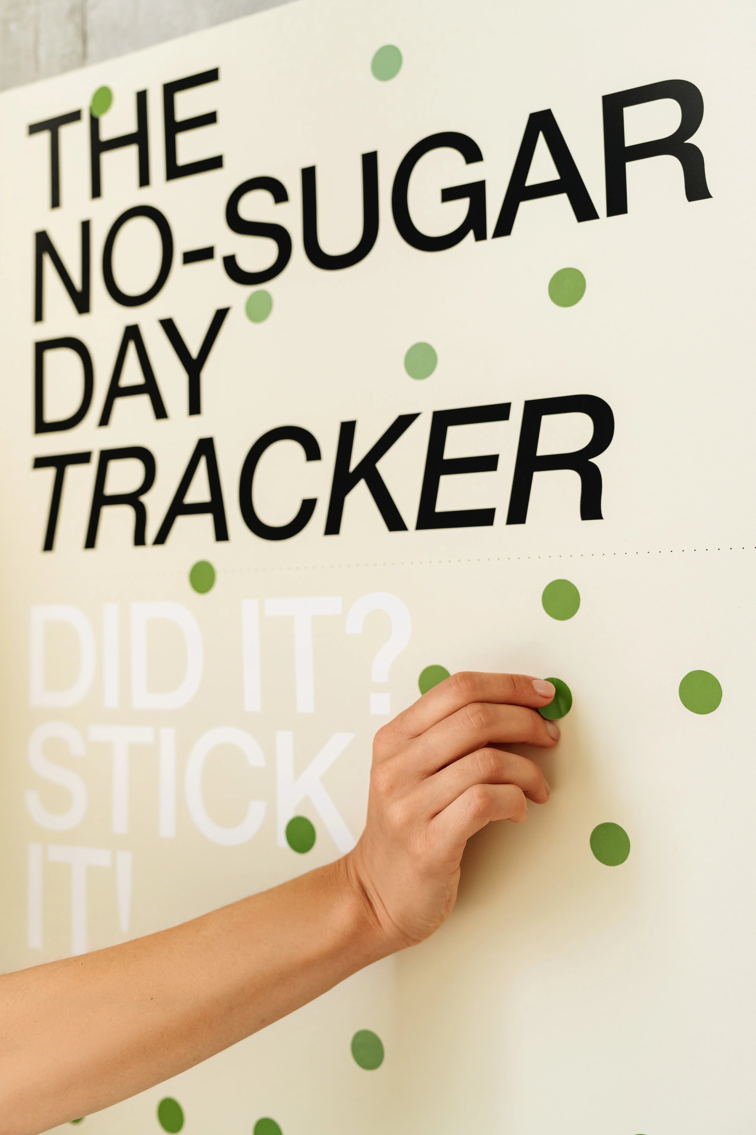 No-Sugar Day Tracker with a hand placing a green sticker on a white background