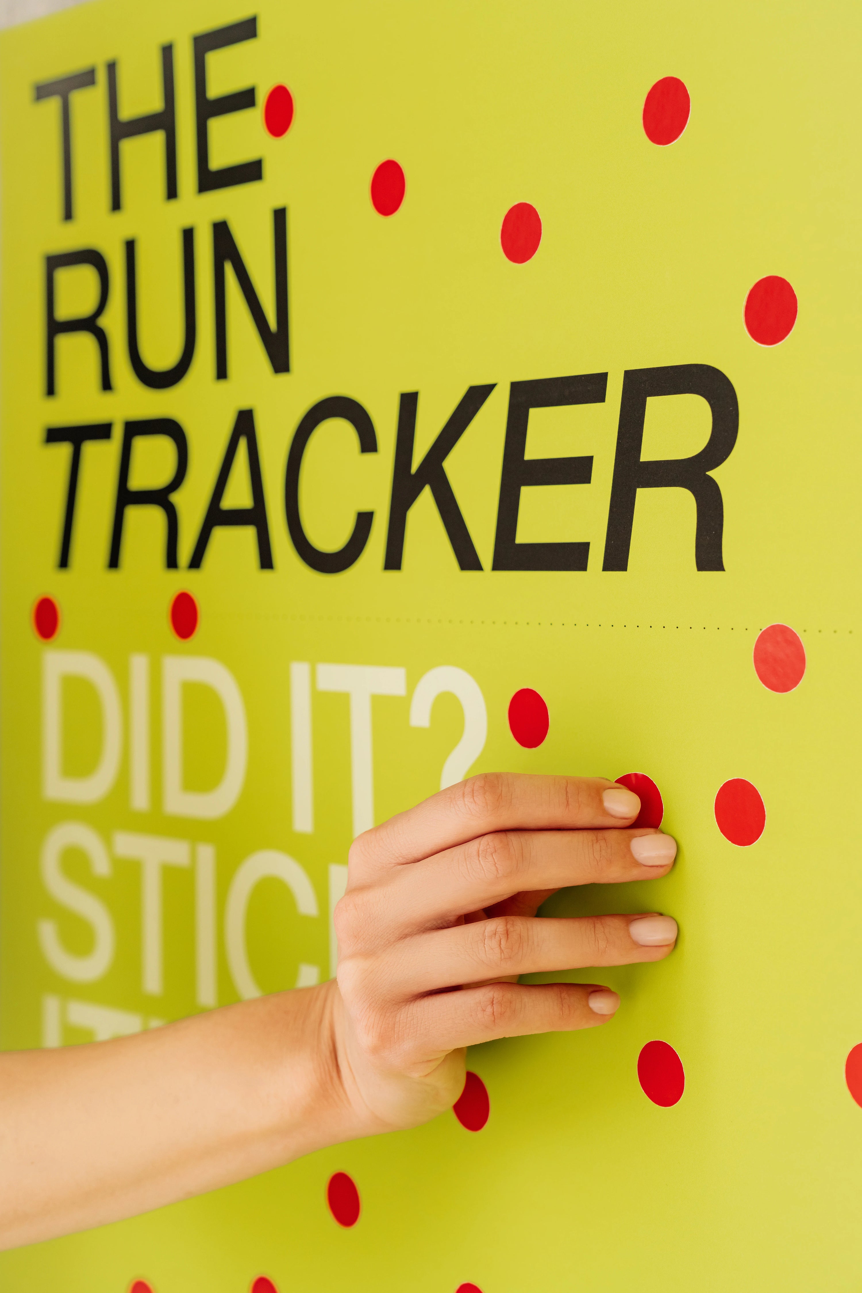 Hand touching a green board with text 'The Run Tracker Did It? Stick' on a yellow background